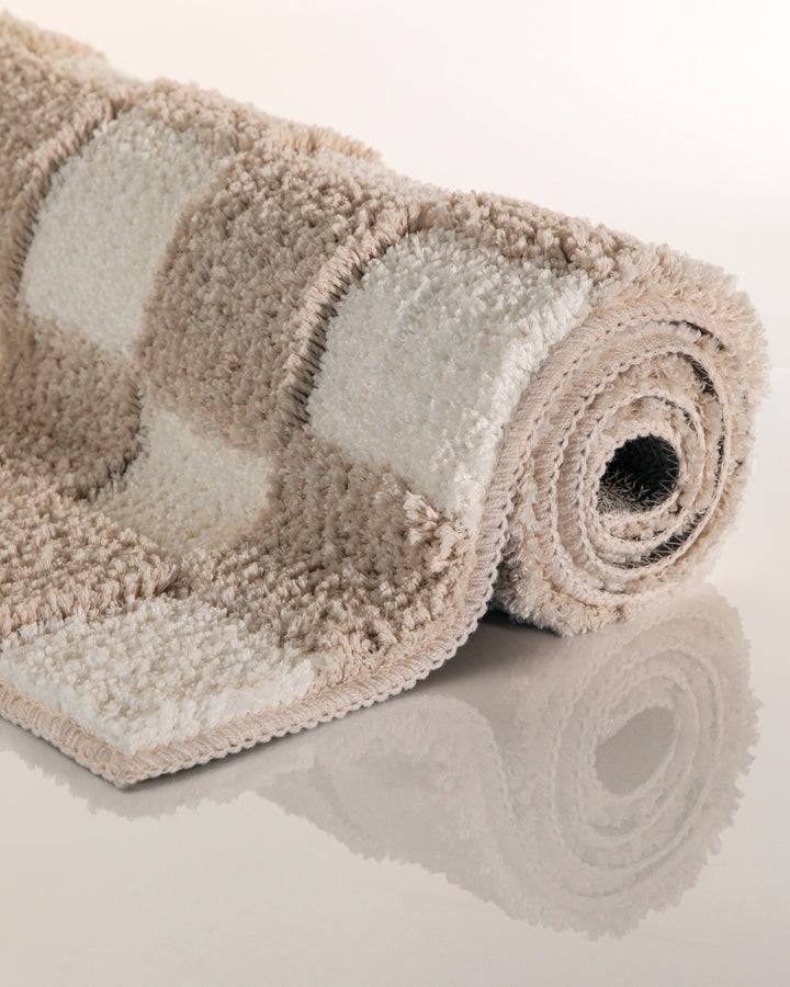 Badteppich Bobbi Beige aufgerollt auf hellem Hintergrund, Seitenansicht zeigt Florhöhe und Musterverlauf