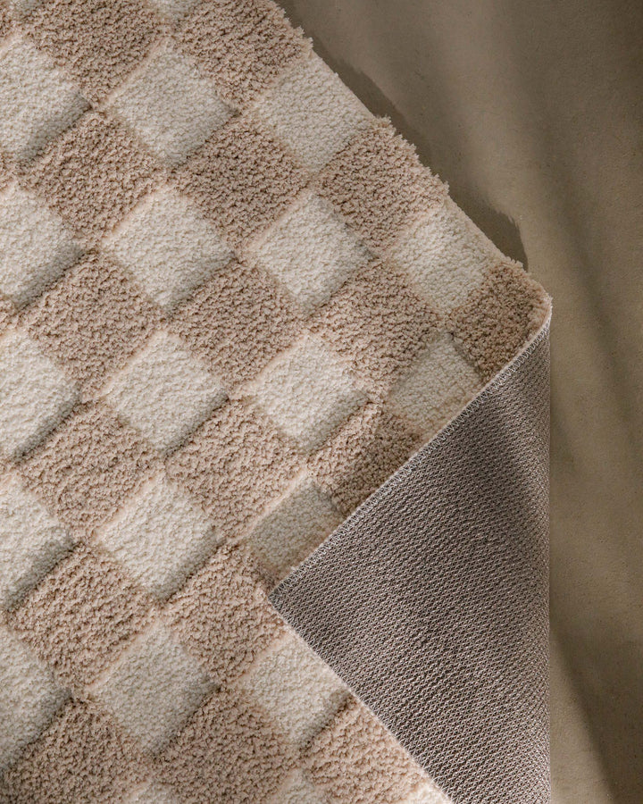 Badteppich Bobbi Beige im Badezimmer vor Holzbank auf hellem Boden, rechteckige Matte mit Schachbrettmuster
