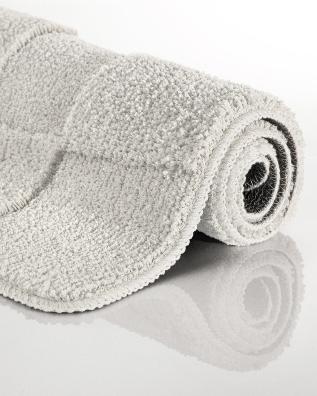 Badteppich Davie Weiß aufgerollt auf hellem Hintergrund, Seitenansicht zeigt Florhöhe und Teppichkante