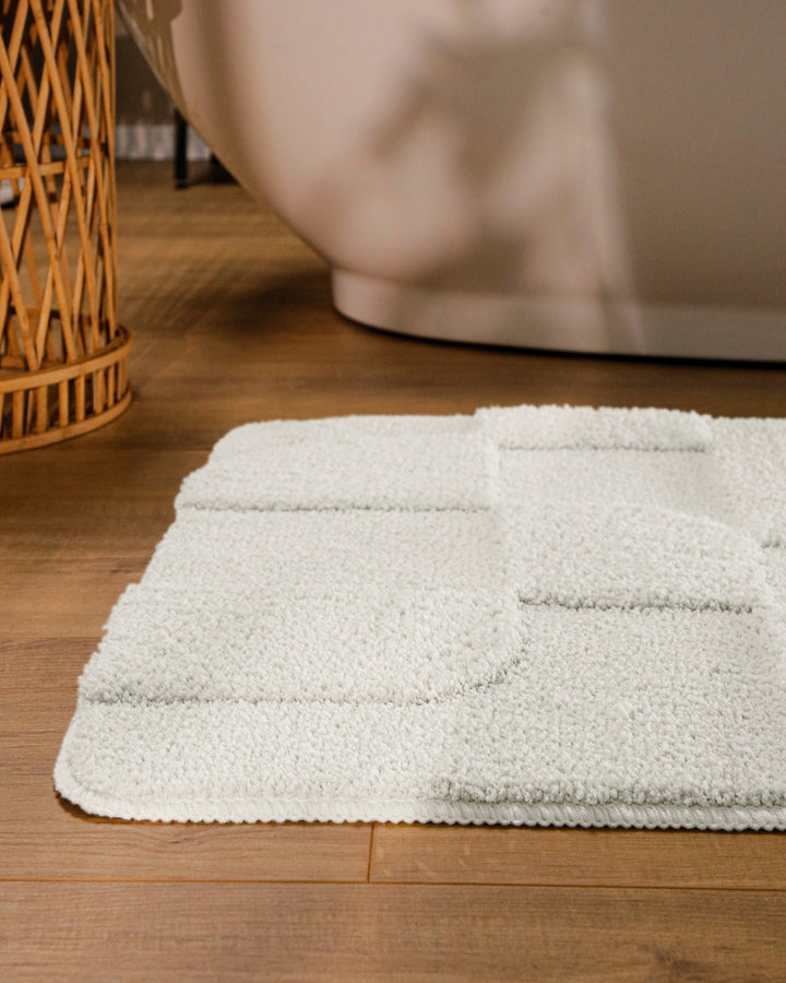 Badteppich Davie Weiß runde Matte im Badezimmer vor Badewanne, Strukturmuster im Flor auf Holzboden sichtbar