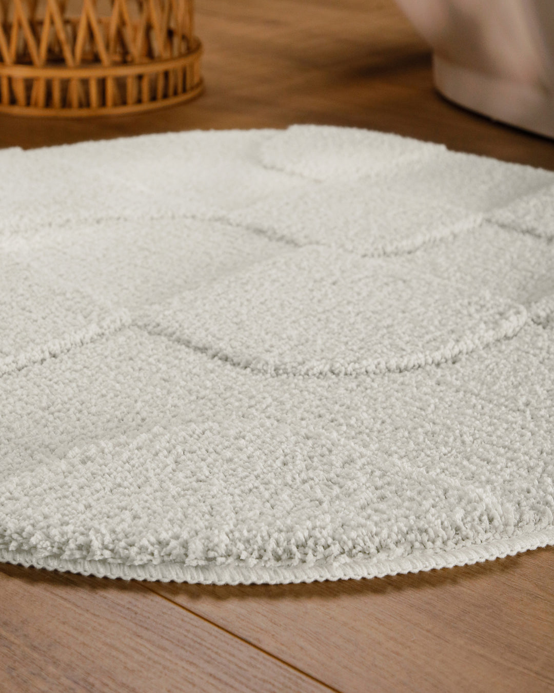 Badteppich Davie Weiß rund im Badezimmer auf Holzboden neben Badewanne, Florstruktur und Linienrelief erkennbar