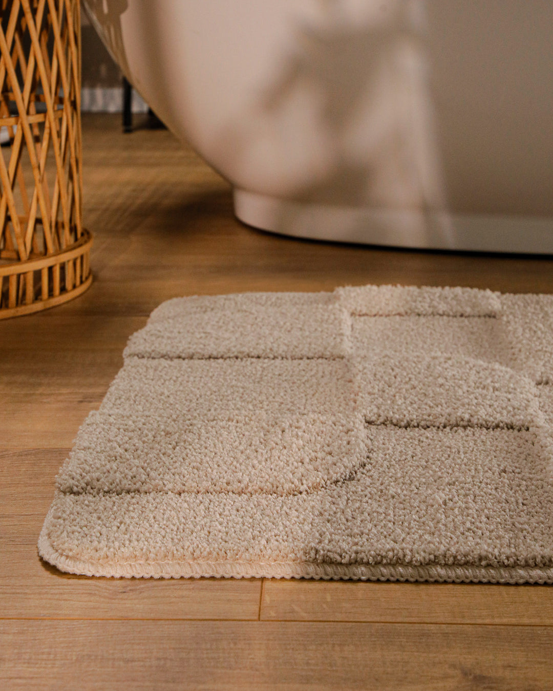 Badteppich Davie Sand Beige runde Matte im Badezimmer vor Badewanne, Strukturmuster im Flor auf Holzboden sichtbar