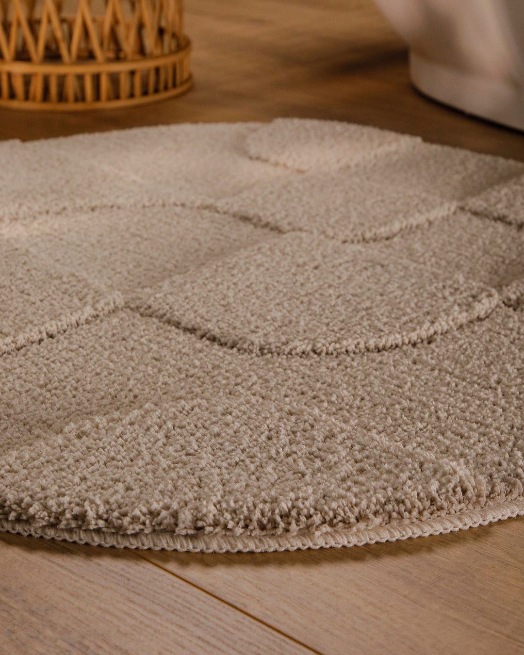 Badteppich Davie Sand Beige rund im Badezimmer auf Holzboden neben Badewanne, Florstruktur und Linienrelief erkennbar