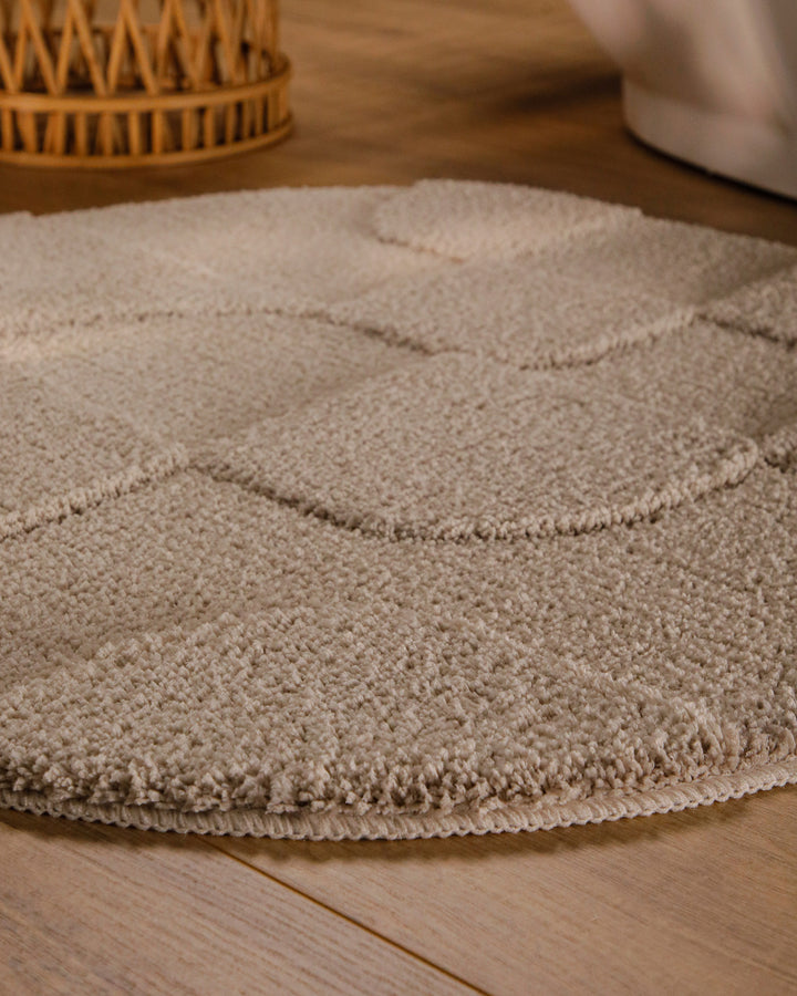 Badteppich Davie Sand Beige rund im Badezimmer auf Holzboden neben Badewanne, Florstruktur und Linienrelief erkennbar