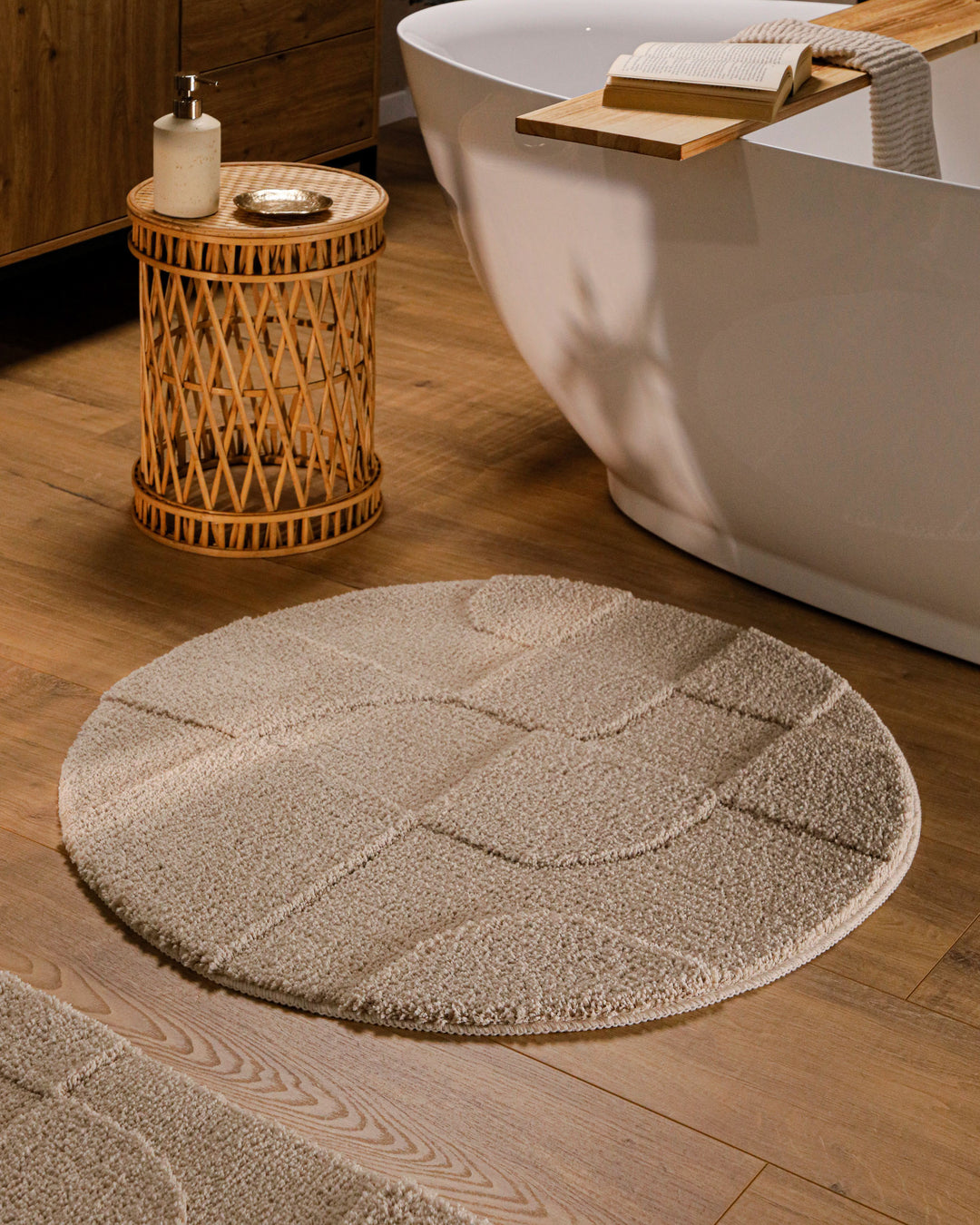 Runder Badteppich Davie Sand Beige im Badezimmer vor Badewanne auf Holzboden, strukturiertes Linienrelief im Flor sichtbar