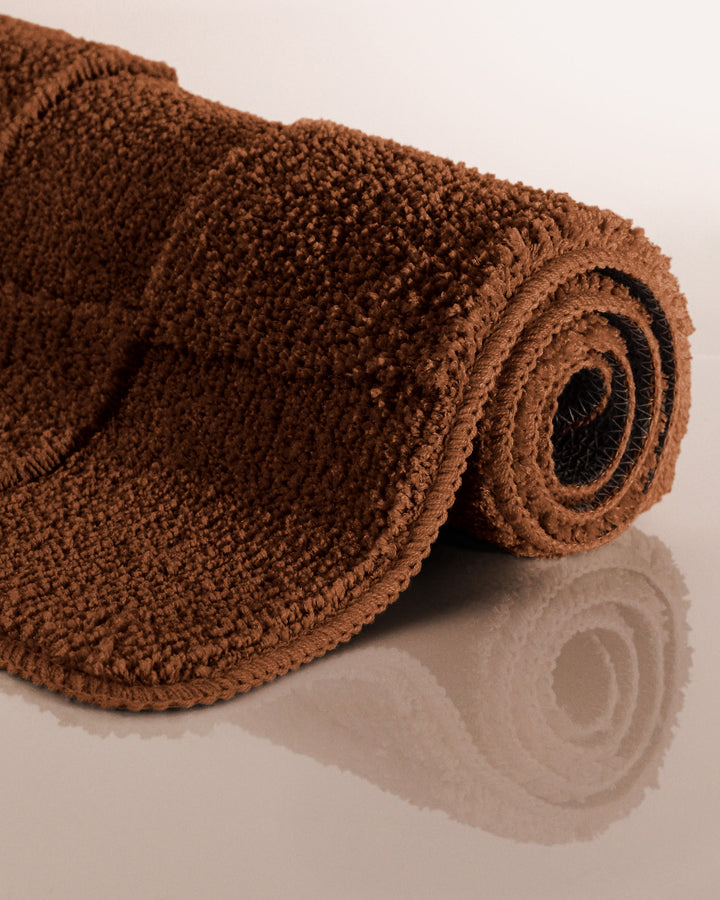 Badteppich Davie Braun aufgerollt auf hellem Hintergrund, Seitenansicht zeigt Florhöhe und Teppichkante