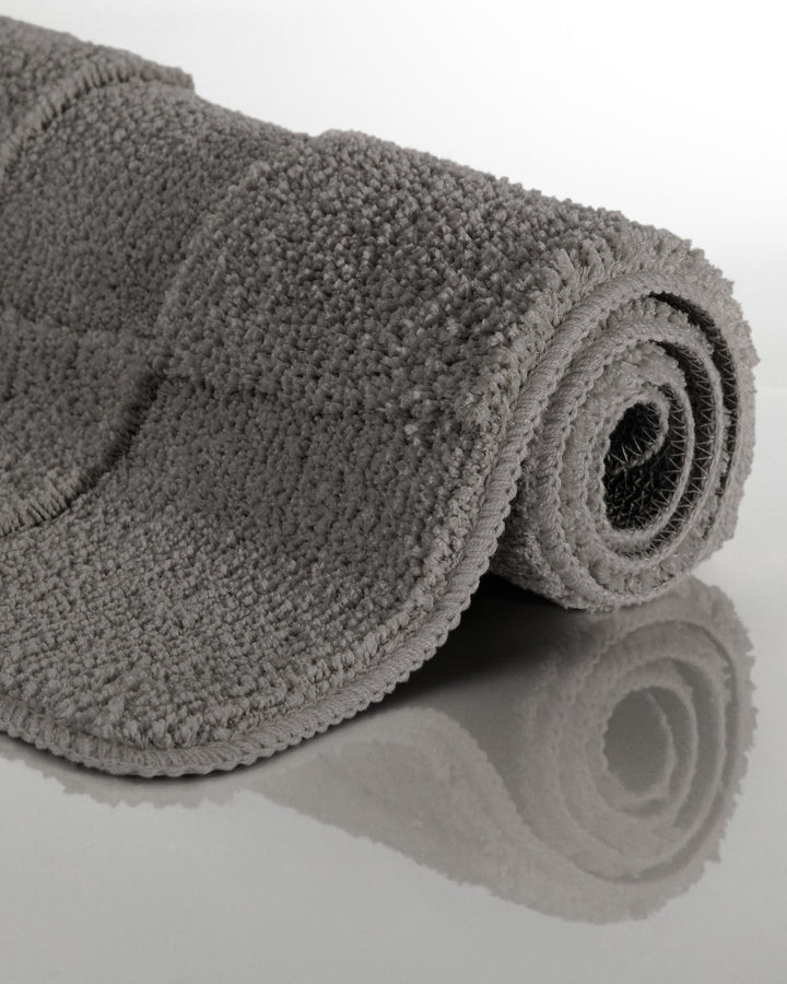 Badteppich Davie Basalt Grau aufgerollt auf hellem Hintergrund, Seitenansicht zeigt Florhöhe und Teppichkante