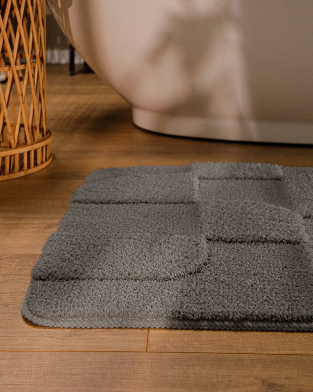 Badteppich Davie Basalt Grau runde Matte im Badezimmer vor Badewanne, Strukturmuster im Flor auf Holzboden sichtbar