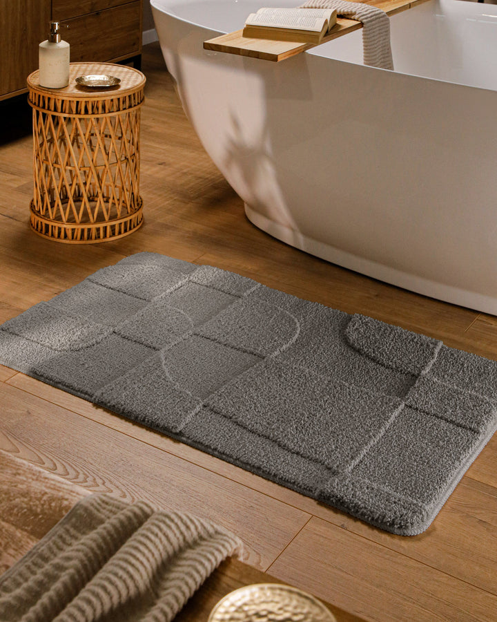 Badteppich Davie Basalt Grau rechteckig im Badezimmer vor Badewanne auf Holzboden liegend, Strukturmuster im Flor sichtbar