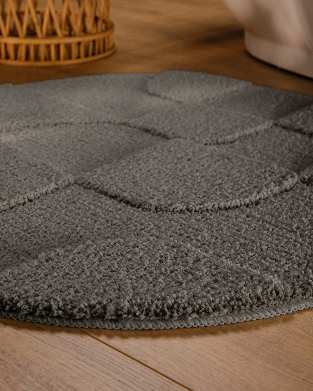 Badteppich Davie Basalt Grau rund im Badezimmer auf Holzboden neben Badewanne, Florstruktur und Linienrelief erkennbar