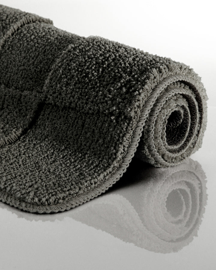 Badteppich Davie Anthrazit Grau aufgerollt auf hellem Hintergrund, Seitenansicht zeigt Florhöhe und Teppichkante