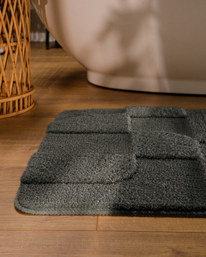 Badteppich Davie Anthrazit Grau runde Matte im Badezimmer vor Badewanne, Strukturmuster im Flor auf Holzboden sichtbar