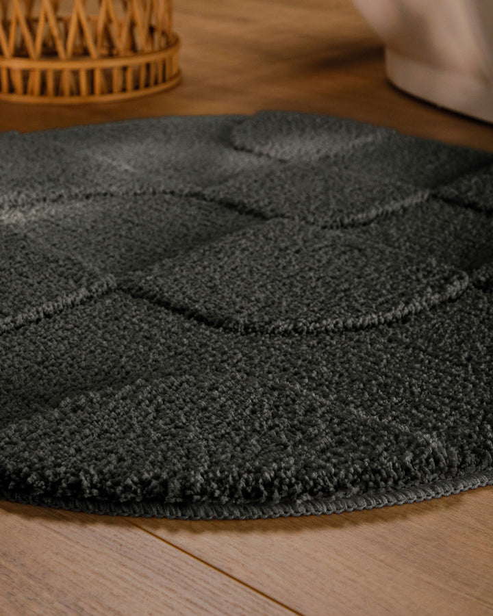 Badteppich Davie Anthrazit Grau rund im Badezimmer auf Holzboden neben Badewanne, Florstruktur und Linienrelief erkennbar