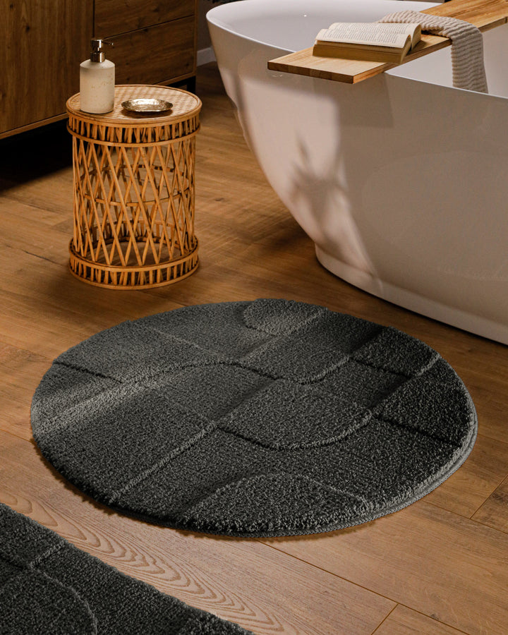Runder Badteppich Davie Anthrazit Grau im Badezimmer vor Badewanne auf Holzboden, strukturiertes Linienrelief im Flor sichtbar