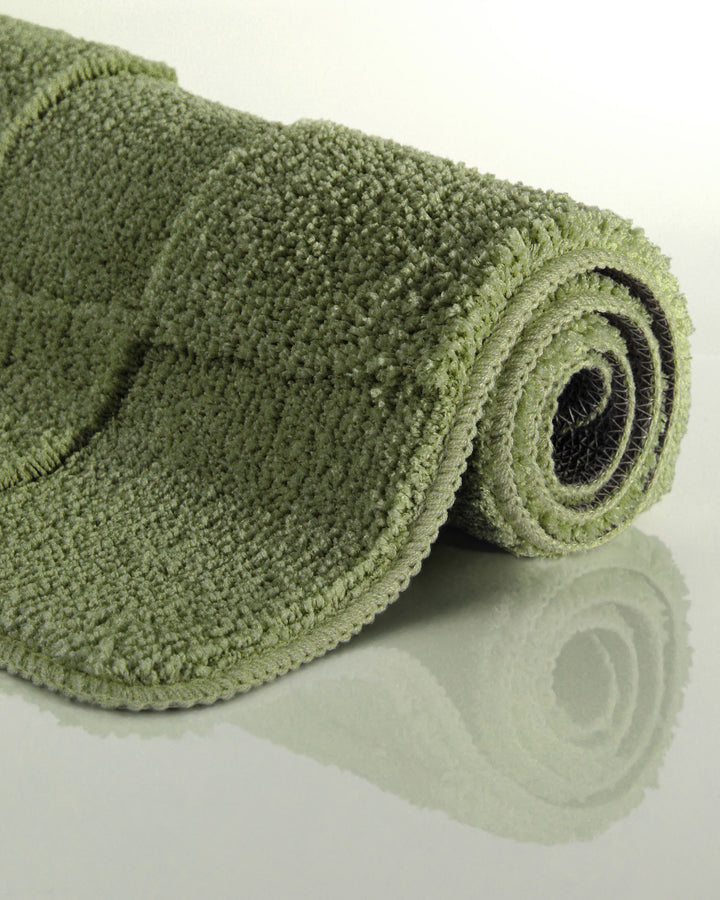 Badteppich Davie Reseda Grün aufgerollt auf hellem Hintergrund, Seitenansicht zeigt Florhöhe und Teppichkante
