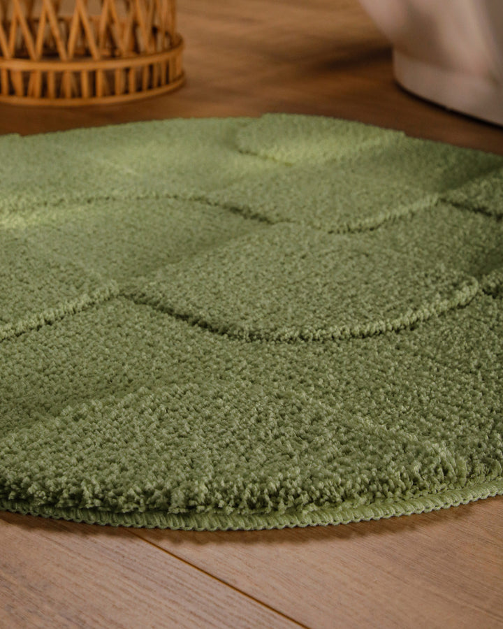 Badteppich Davie Reseda Grün rund im Badezimmer auf Holzboden neben Badewanne, Florstruktur und Linienrelief erkennbar