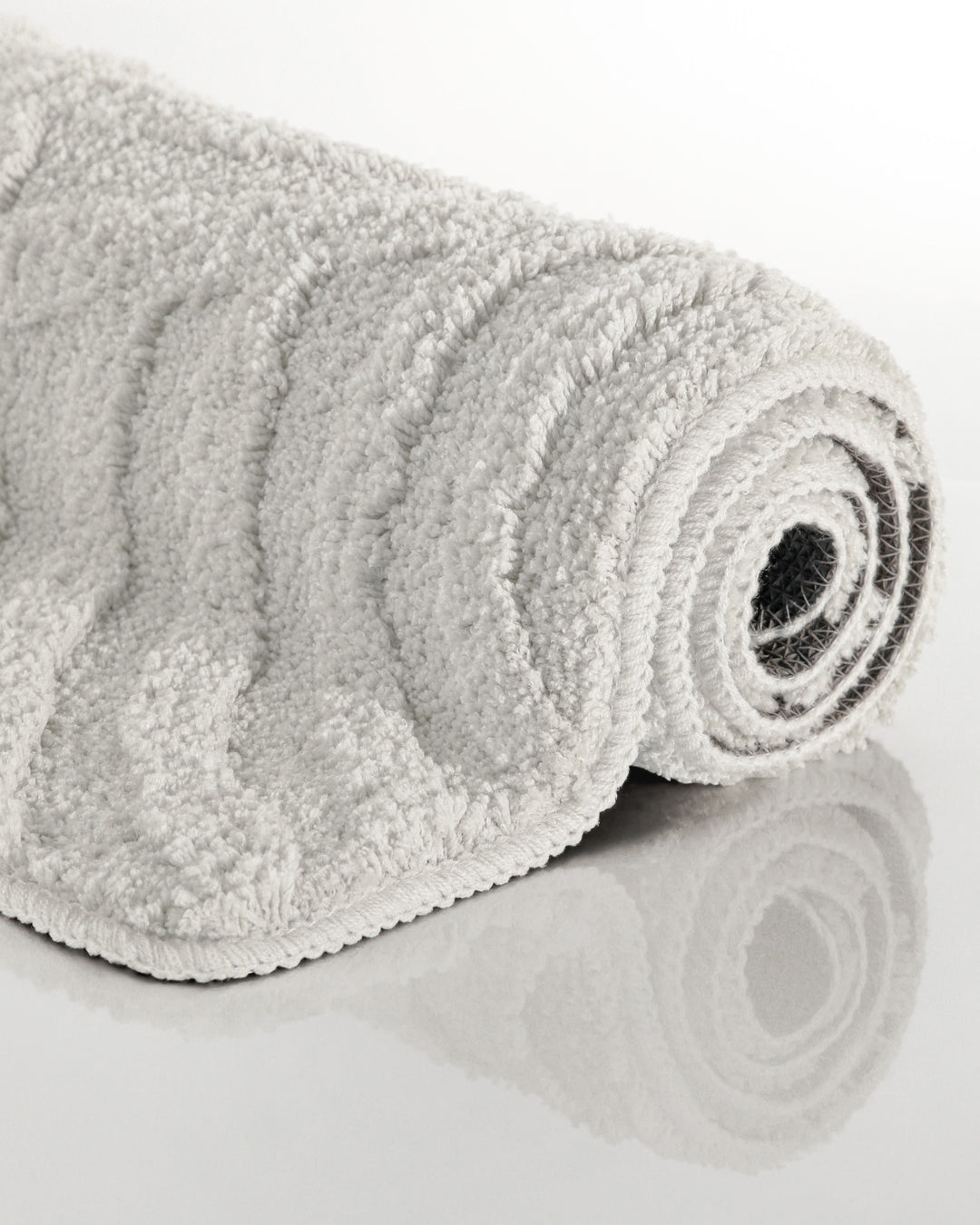 Badteppich Fiete Weiß aufgerollt auf hellem Hintergrund, Seitenansicht zeigt Florhöhe und Teppichkante