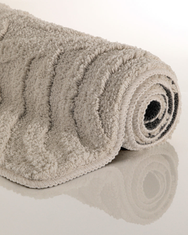 Badteppich Fiete Grau aufgerollt auf hellem Hintergrund, Seitenansicht zeigt Florhöhe und Teppichkante