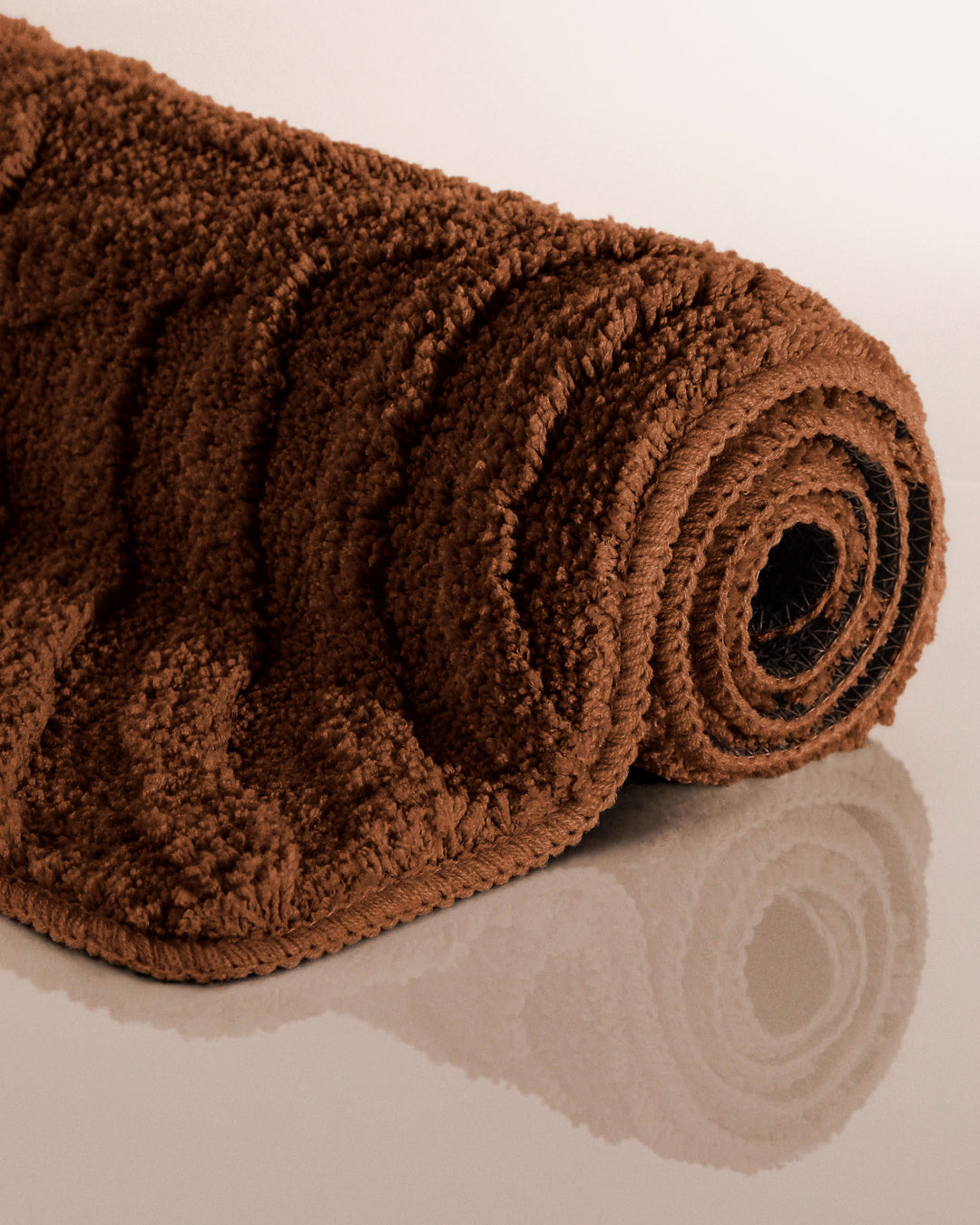 Badteppich Fiete Braun aufgerollt auf hellem Hintergrund, Seitenansicht zeigt Florhöhe und Teppichkante