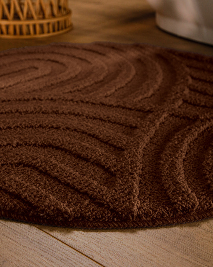 Badteppich Fiete Braun rund im Badezimmer auf Holzboden neben Badewanne, Florstruktur und Linienrelief erkennbar