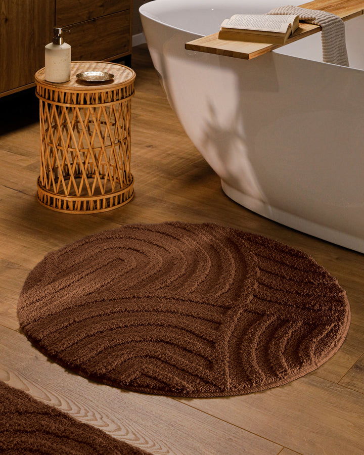 Runder Badteppich Fiete Braun im Badezimmer vor Badewanne auf Holzboden, strukturiertes Linienrelief im Flor sichtbar