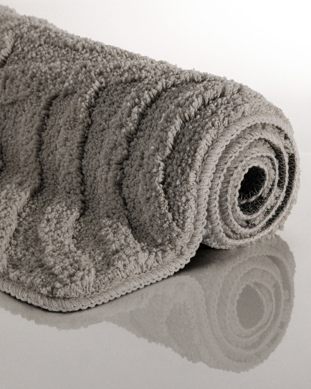 Badteppich Fiete Basalt Grau aufgerollt auf hellem Hintergrund, Seitenansicht zeigt Florhöhe und Teppichkante