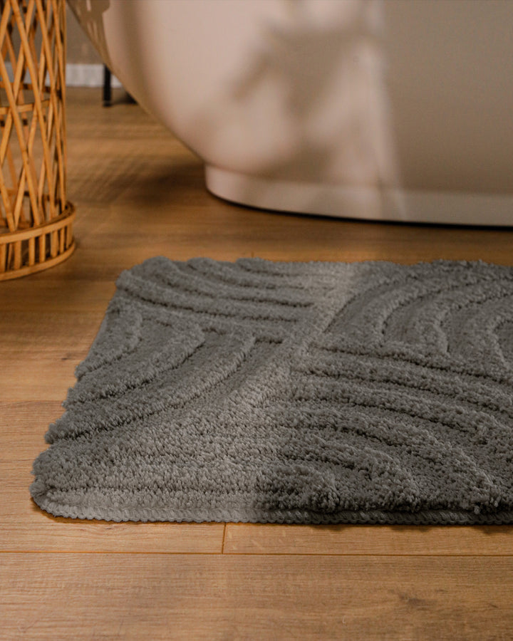 Badteppich Fiete Basalt Grau runde Matte im Badezimmer vor Badewanne, Strukturmuster im Flor auf Holzboden sichtbar