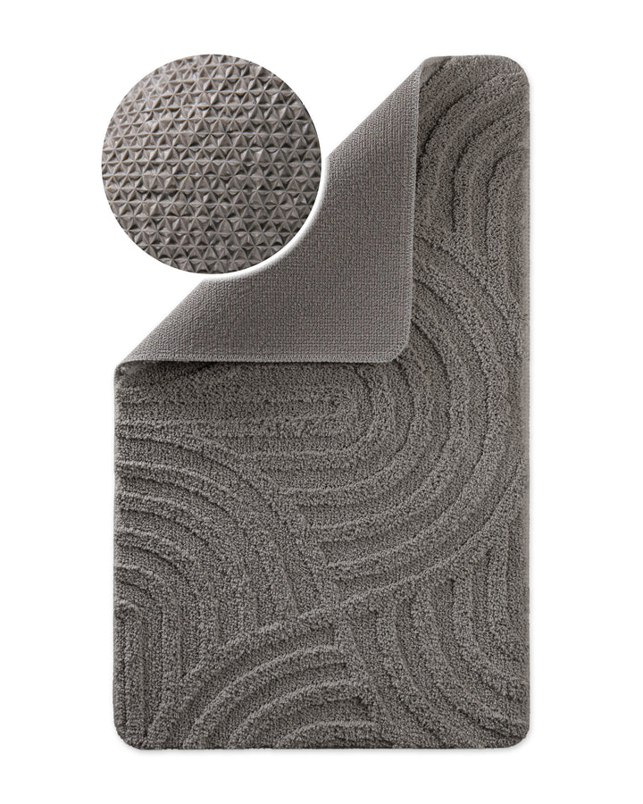 Badteppich Fiete Basalt Grau Ecke hochgeklappt, runde Probe zeigt Basalt Graue Rückseite mit rutschhemmender Beschichtung