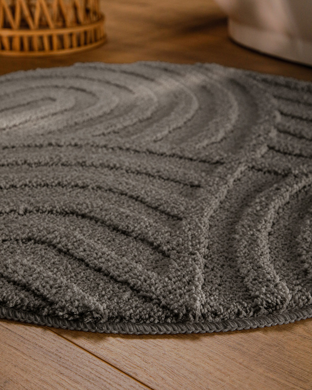 Badteppich Fiete Basalt Grau rund im Badezimmer auf Holzboden neben Badewanne, Florstruktur und Linienrelief erkennbar