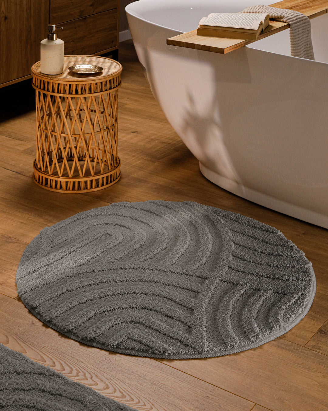 Runder Badteppich Fiete Basalt Grau im Badezimmer vor Badewanne auf Holzboden, strukturiertes Linienrelief im Flor sichtbar