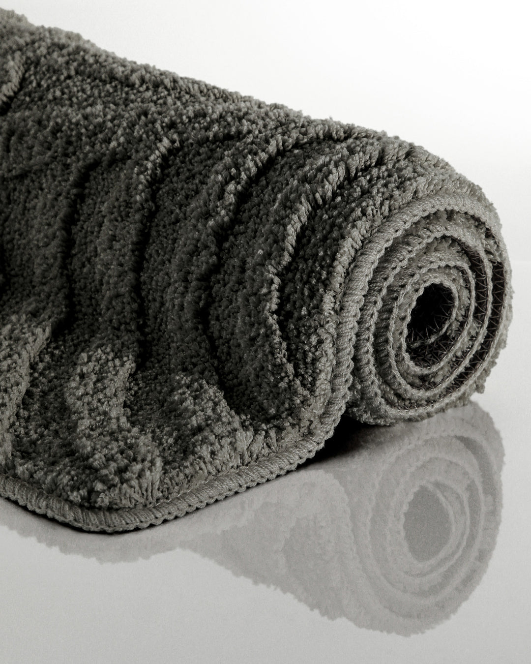Badteppich Fiete Anthrazit Grau aufgerollt auf hellem Hintergrund, Seitenansicht zeigt Florhöhe und Teppichkante