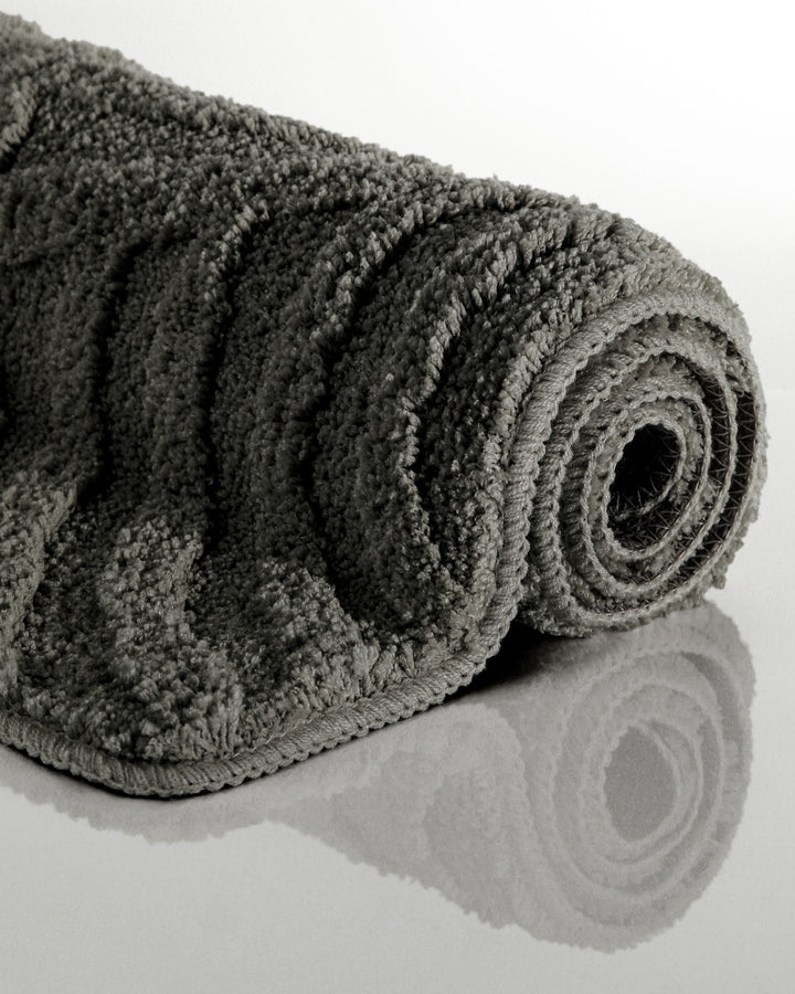 Badteppich Fiete Anthrazit Grau aufgerollt auf hellem Hintergrund, Seitenansicht zeigt Florhöhe und Teppichkante