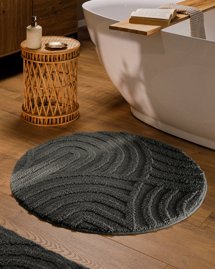 Runder Badteppich Fiete Anthrazit Grau im Badezimmer vor Badewanne auf Holzboden, strukturiertes Linienrelief im Flor sichtbar