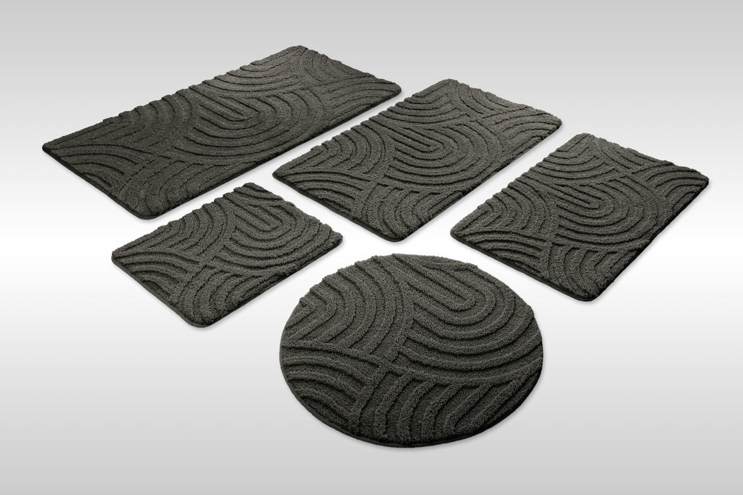 Badteppich Fiete Anthrazit Grau Set aus rechteckigen und runden Badmatten, mehrere Größen auf hellem Hintergrund angeordnet