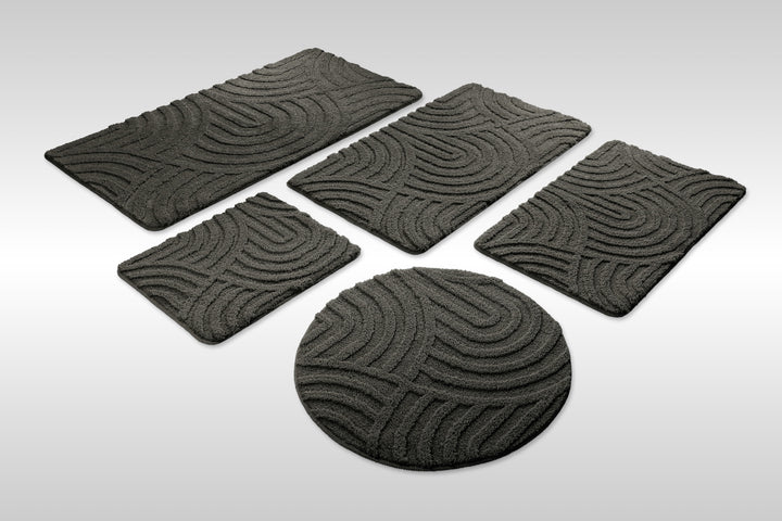 Badteppich Fiete Anthrazit Grau Set aus rechteckigen und runden Badmatten, mehrere Größen auf hellem Hintergrund angeordnet