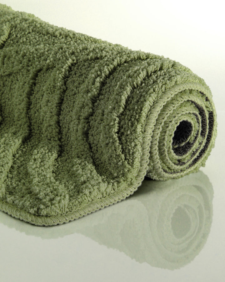 Badteppich Fiete Reseda Grün aufgerollt auf hellem Hintergrund, Seitenansicht zeigt Florhöhe und Teppichkante