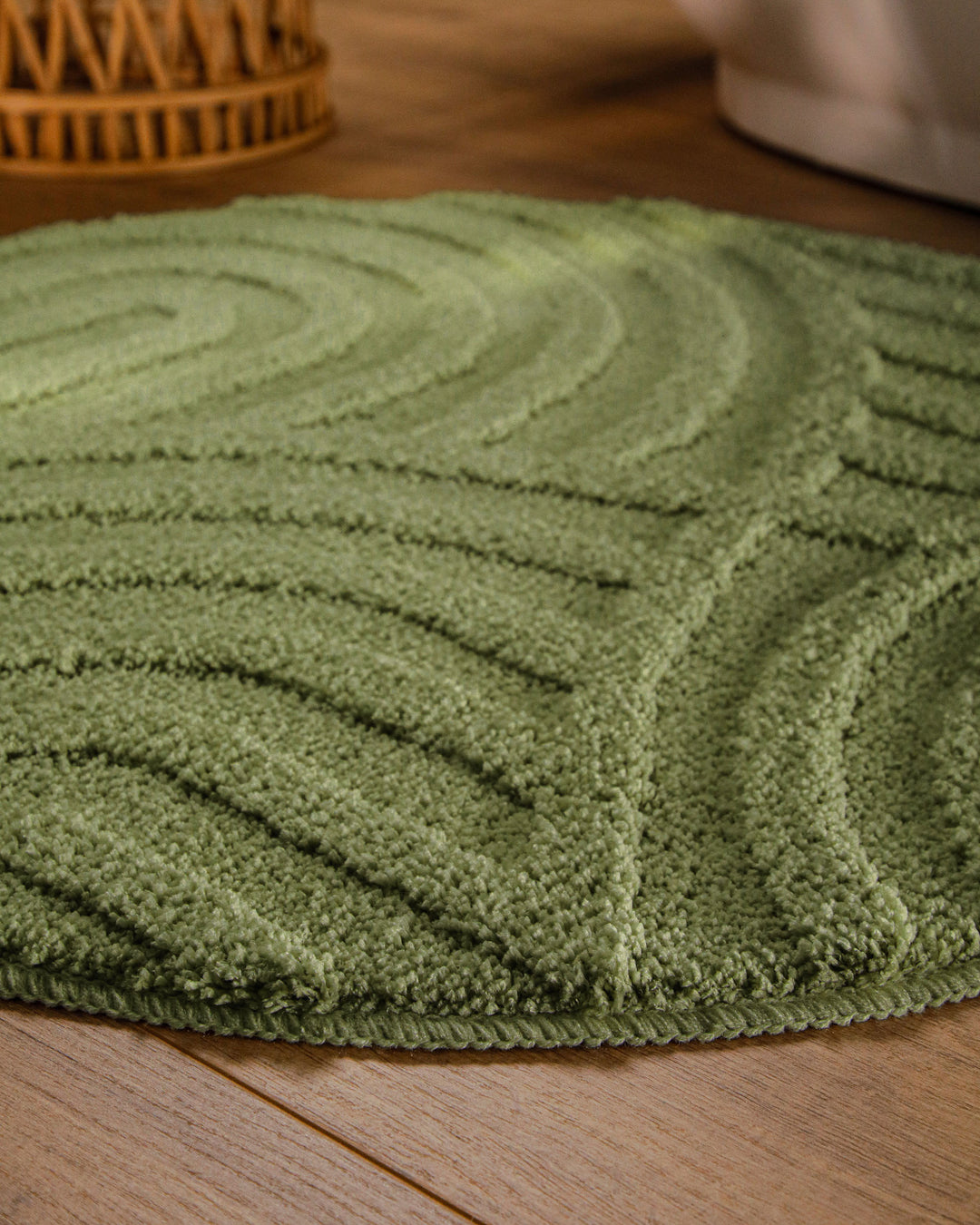 Badteppich Fiete Reseda Grün rund im Badezimmer auf Holzboden neben Badewanne, Florstruktur und Linienrelief erkennbar