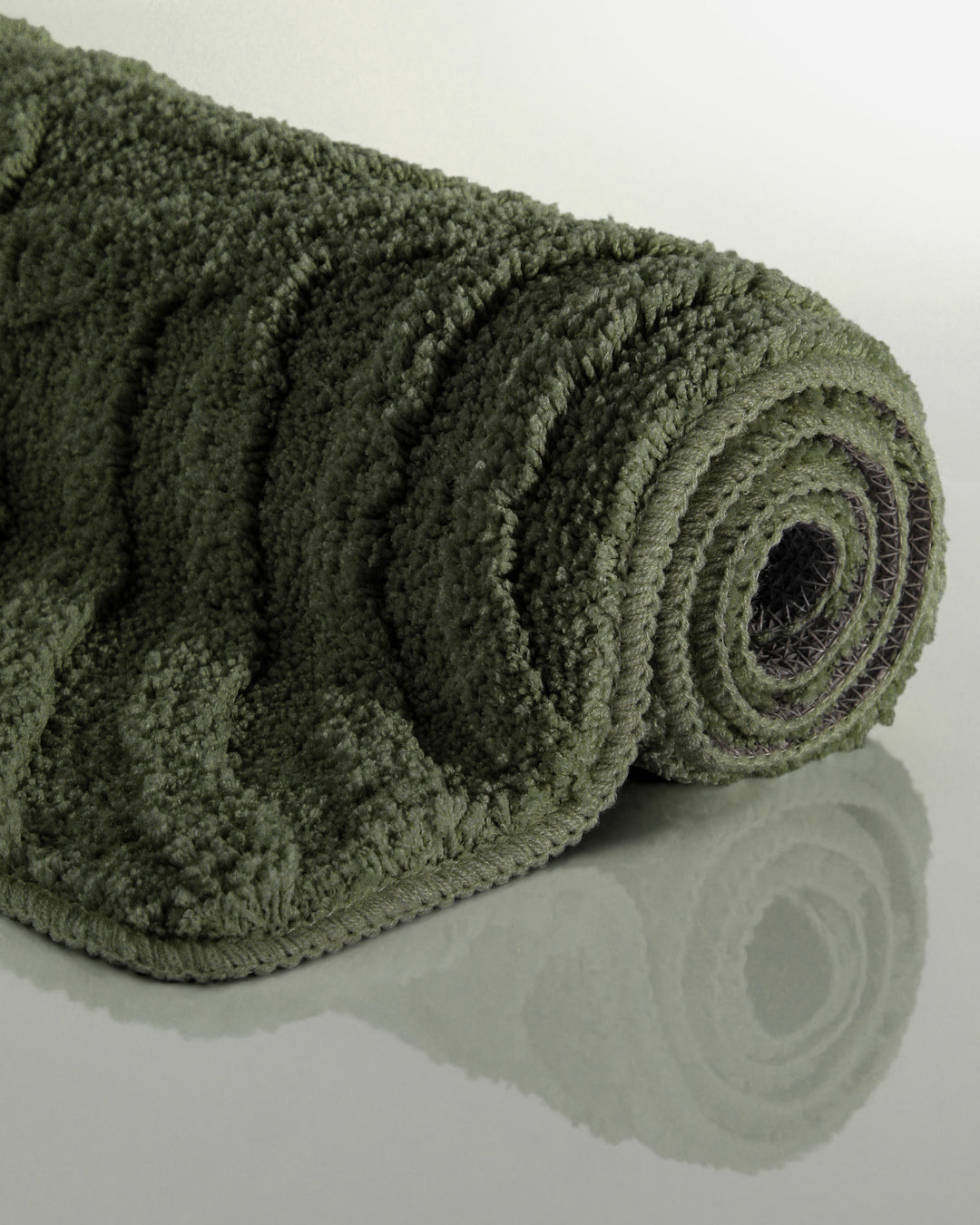 Badteppich Fiete Kiefer Grün aufgerollt auf hellem Hintergrund, Seitenansicht zeigt Florhöhe und Teppichkante