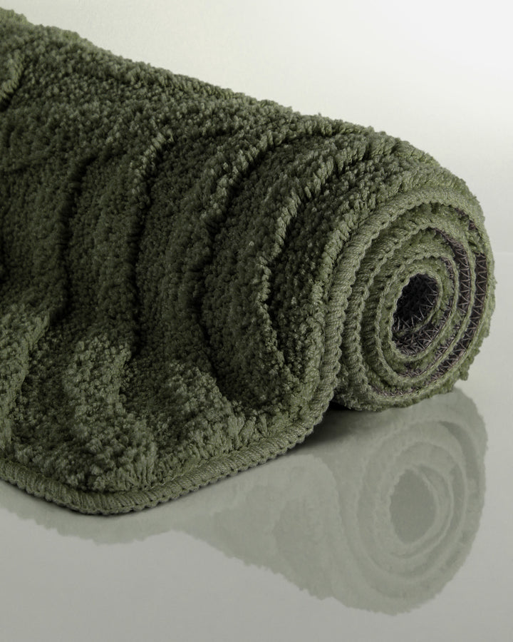 Badteppich Fiete Kiefer Grün aufgerollt auf hellem Hintergrund, Seitenansicht zeigt Florhöhe und Teppichkante