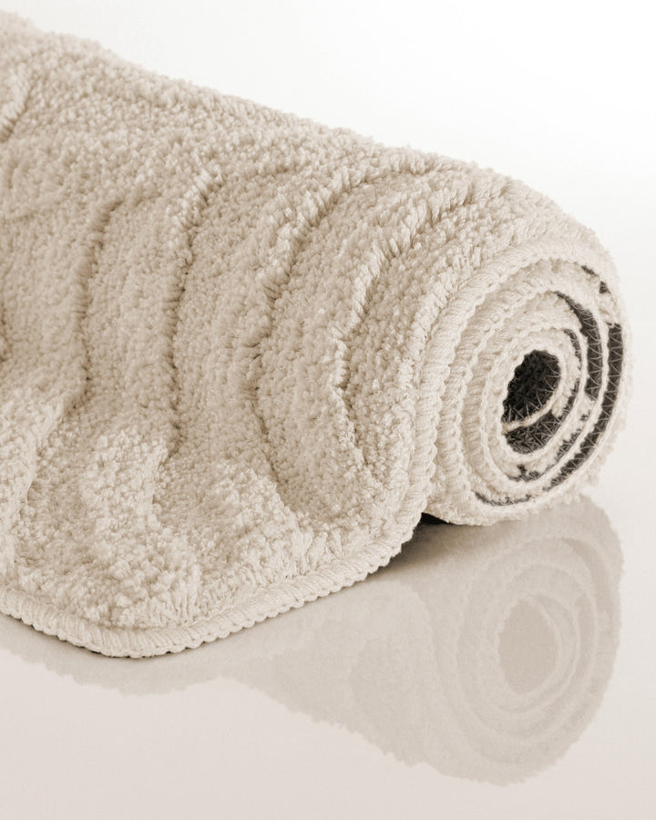 Badteppich Fiete Creme Weiß aufgerollt auf hellem Hintergrund, Seitenansicht zeigt Florhöhe und Teppichkante
