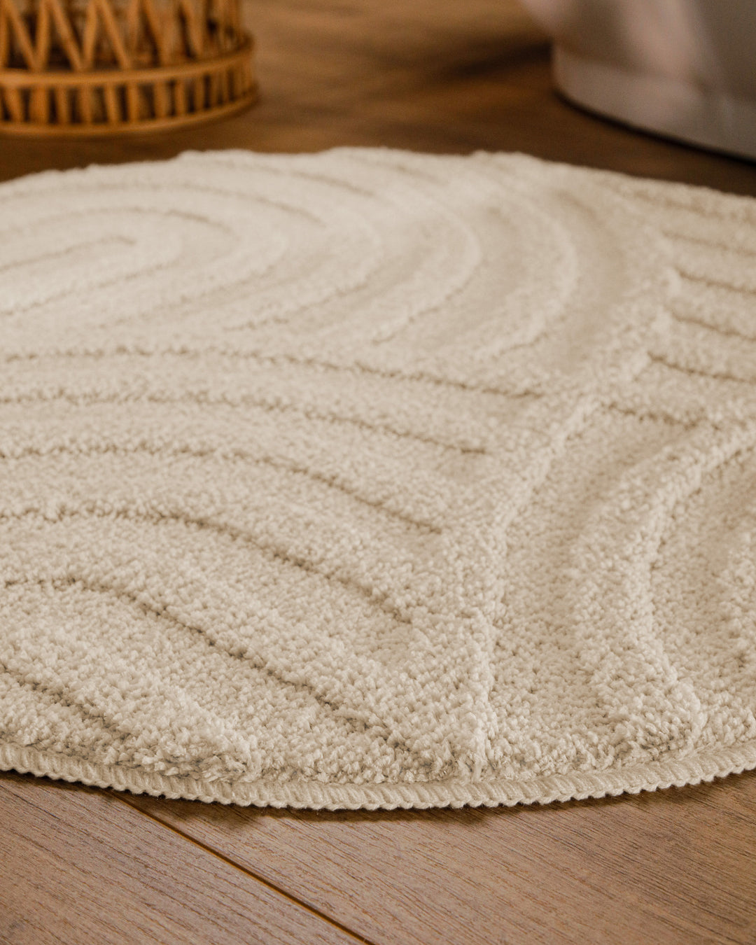 Badteppich Fiete Creme Weiß rund im Badezimmer auf Holzboden neben Badewanne, Florstruktur und Linienrelief erkennbar