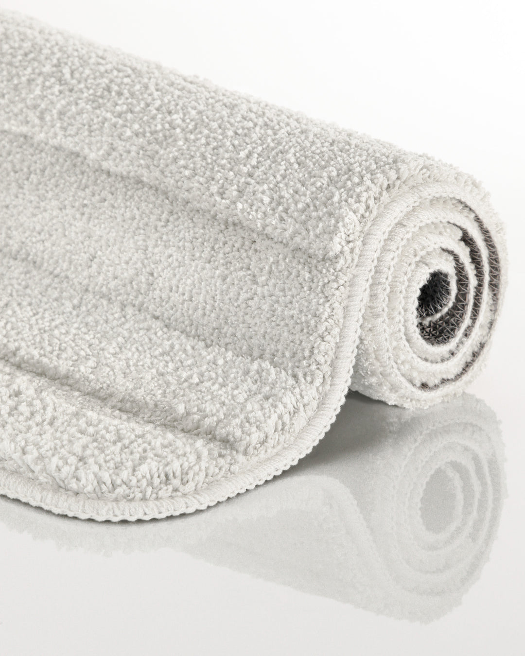 Badteppich Marc Weiß aufgerollt auf hellem Hintergrund, Seitenansicht zeigt Florhöhe und Teppichkante
