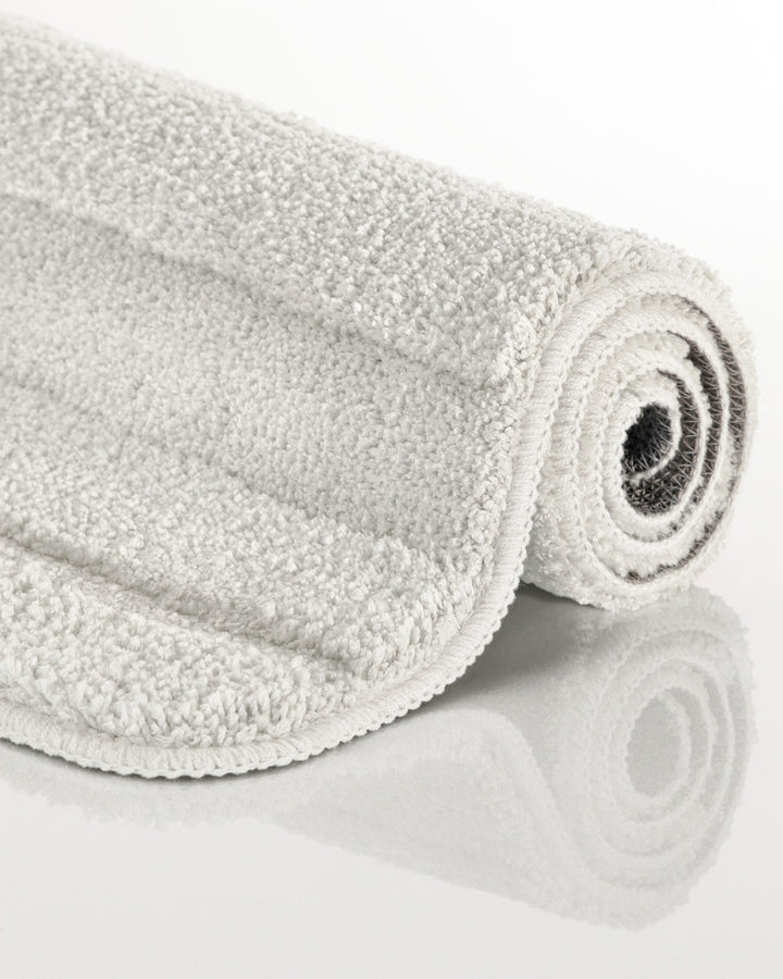 Badteppich Marc Weiß aufgerollt auf hellem Hintergrund, Seitenansicht zeigt Florhöhe und Teppichkante
