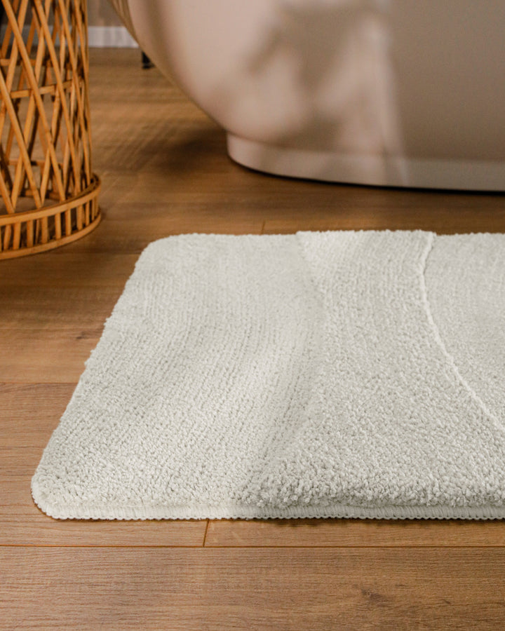 Badteppich Marc Weiß runde Matte im Badezimmer vor Badewanne, Strukturmuster im Flor auf Holzboden sichtbar