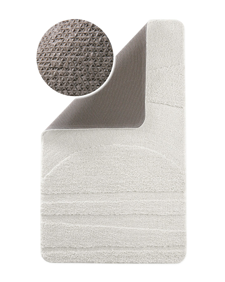 Badteppich Marc Weiß Ecke hochgeklappt, runde Probe zeigt graue Rückseite mit rutschhemmender Beschichtung