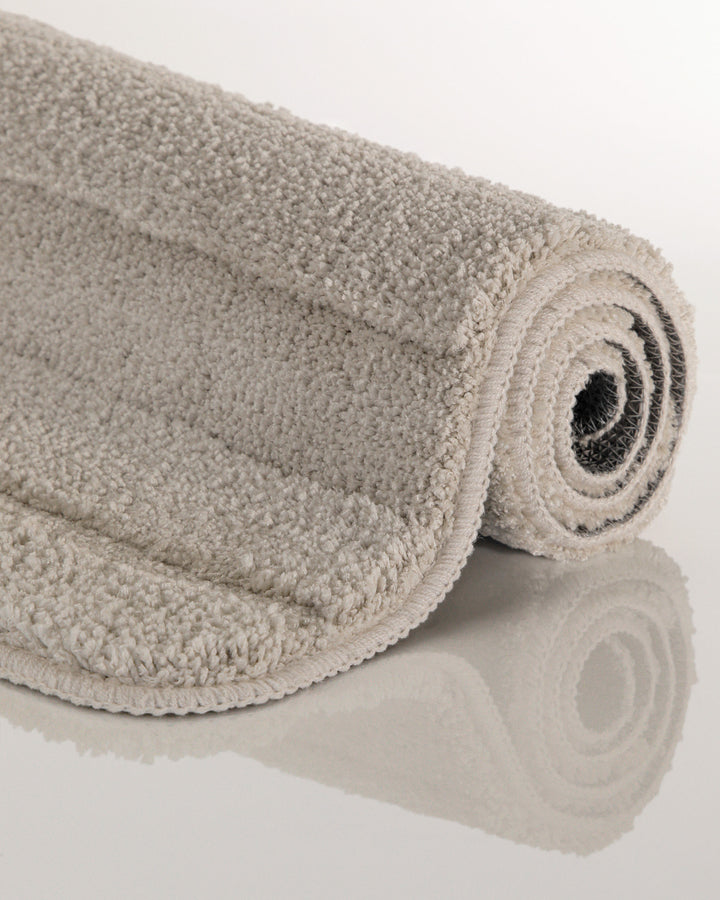 Badteppich Marc Grau aufgerollt auf hellem Hintergrund, Seitenansicht zeigt Florhöhe und Teppichkante