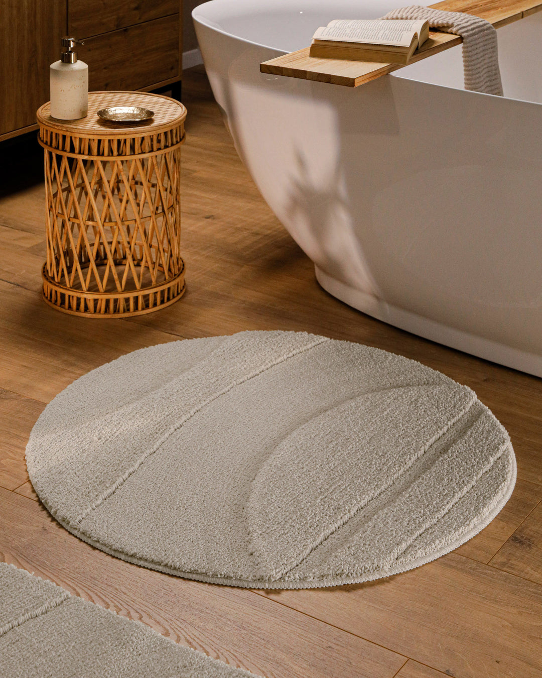 Runder Badteppich Marc Grau im Badezimmer vor Badewanne auf Holzboden, strukturiertes Linienrelief im Flor sichtbar