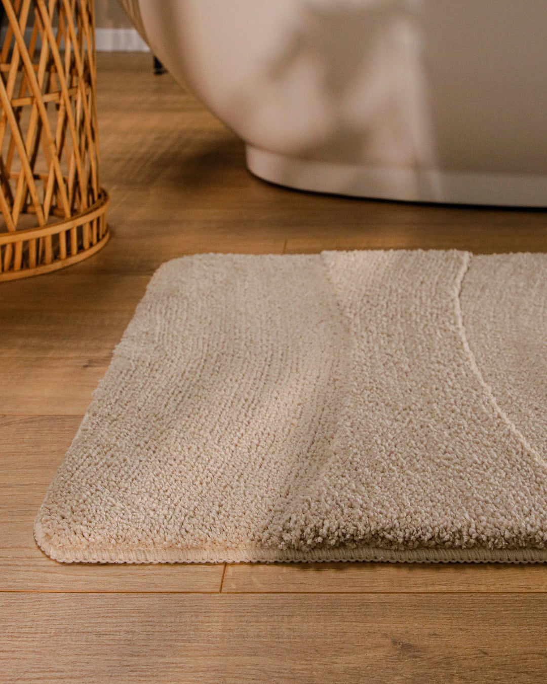 Badteppich Marc Sand Beige runde Matte im Badezimmer vor Badewanne, Strukturmuster im Flor auf Holzboden sichtbar