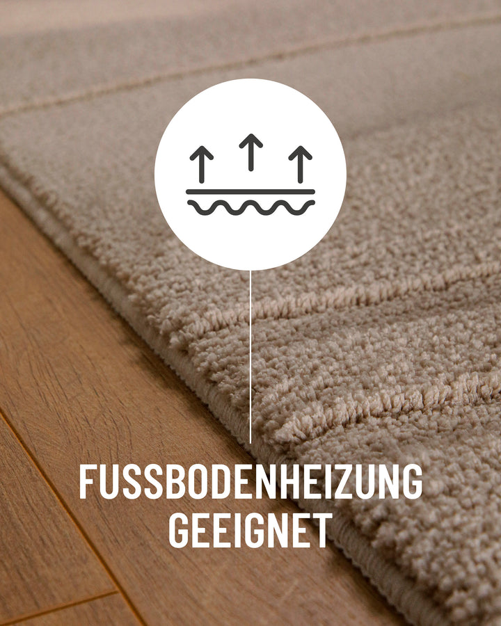 Badteppich Marc Sand Beige Detail auf Holzfußboden mit Symbol für Fußbodenheizung, Nahaufnahme von Flor und Teppichkante