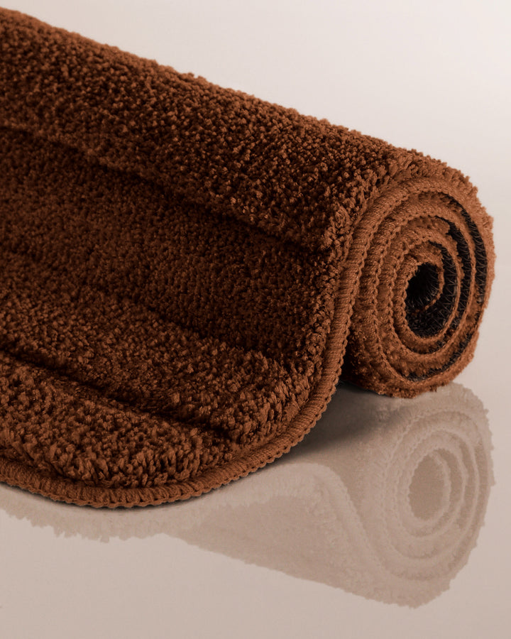 Badteppich Marc Braun aufgerollt auf hellem Hintergrund, Seitenansicht zeigt Florhöhe und Teppichkante